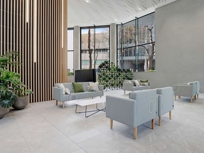 Modern lobby with light gray seating, wooden slat wall, and potted plants at UniLodge Auckland Central.