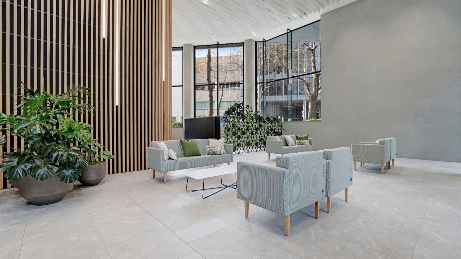 Modern lobby with light gray seating, wooden slat wall, and potted plants at UniLodge Auckland Central.