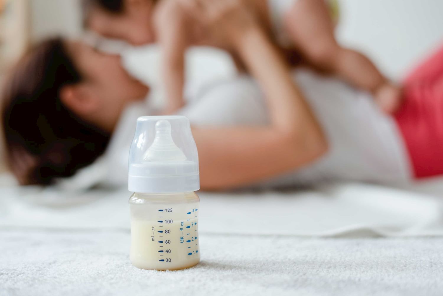 Mother playing with baby on bed with a feeding bottle aside