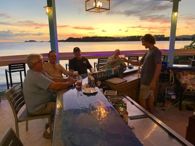 Guests enjoying drinks at a lively outdoor waterfront bar during a vibrant sunset at Emerald Beach Resort