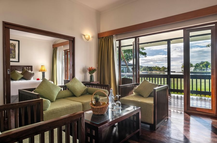 Living area with couch, coffee table, and balcony overlooking a lush landscape at The Naviti Resort.