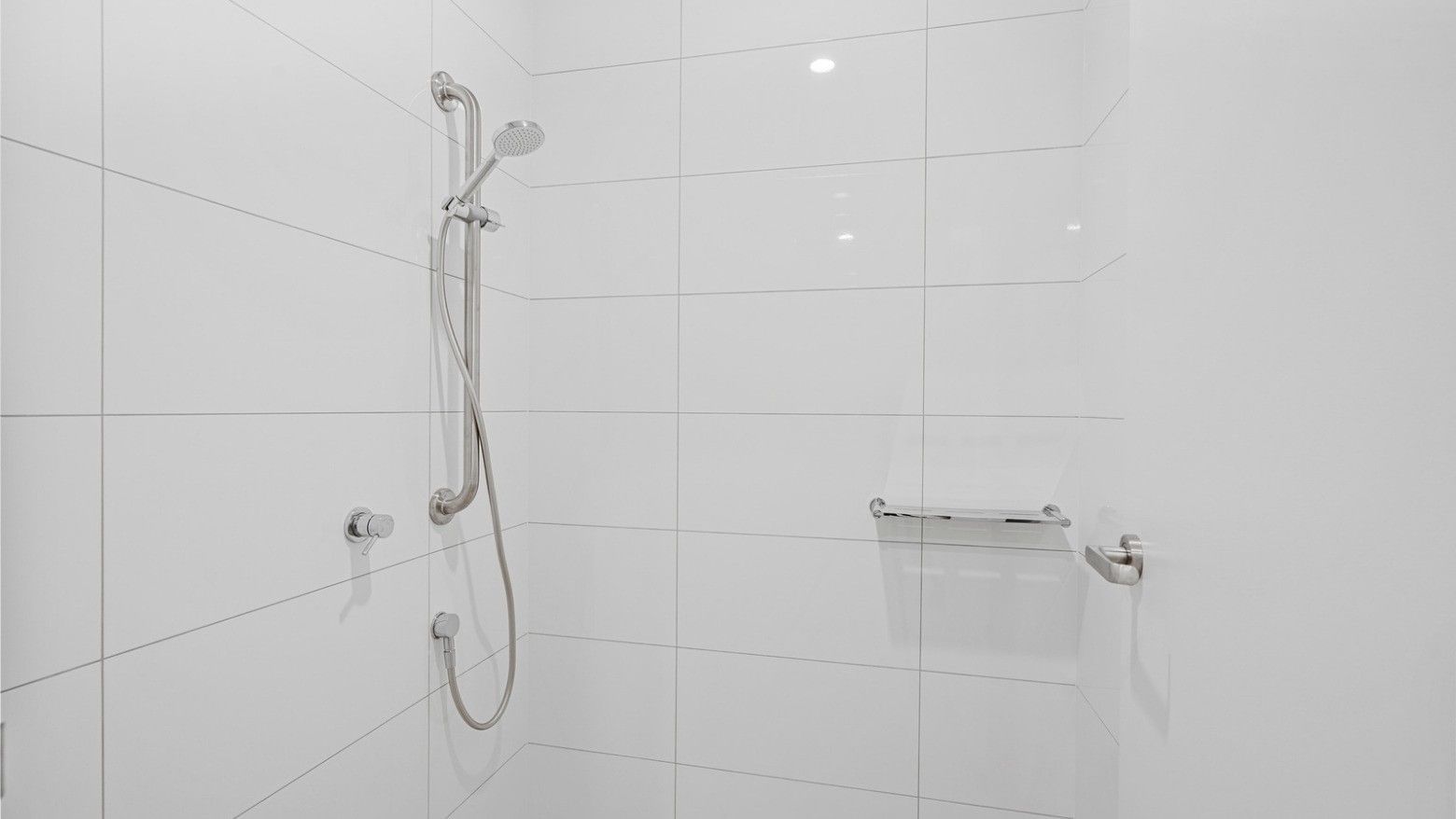 White shower with tiled walls and showerhead at UniLodge Brisbane City.