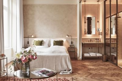 Deluxe Room featuring a bed with green cushions, a floral vase, and a vanity with warm lighting at Hotel Motto Vienna