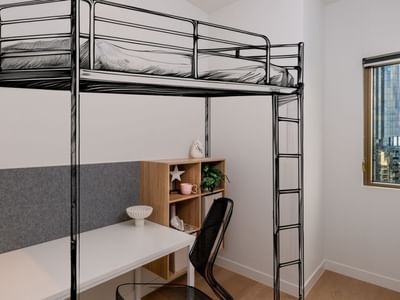 Modern room with bunk bed, desk, chair, and cityscape view at UniLodge Brisbane City.
