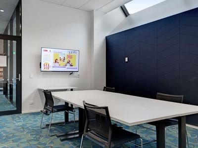 Modern meeting room with white table, black chairs, wall-mounted screen, and blue accent wall at UniLodge Auckland Central.