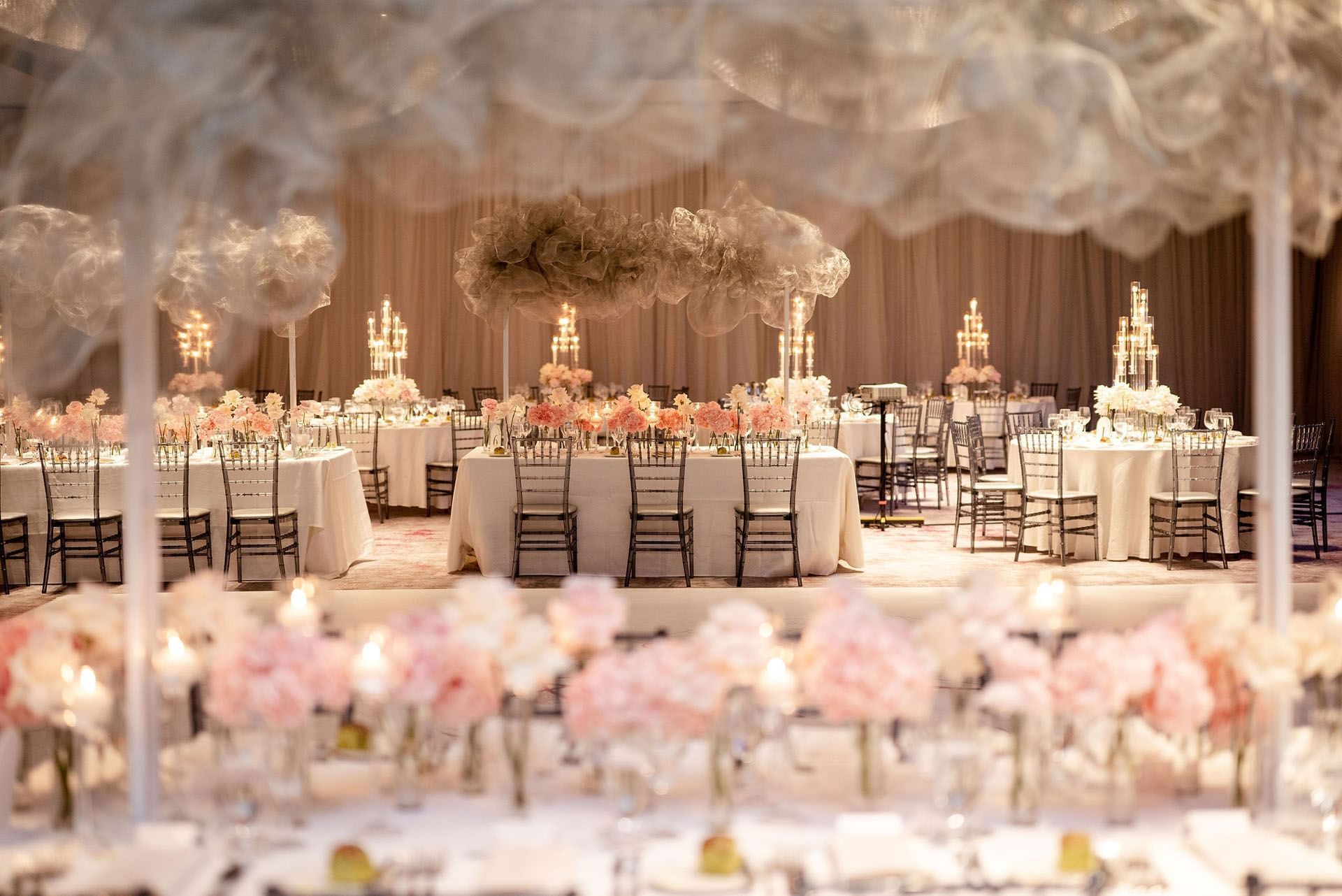 Wedding tables with pink florals and candles under sheer cloud decor, surrounded by chiavari chairs at Hotel X Toronto