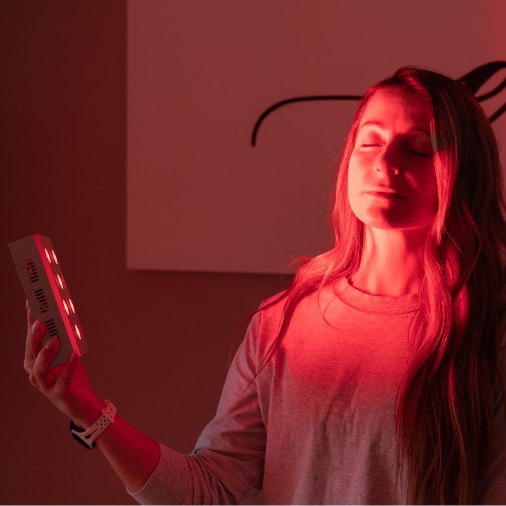 Woman holding a portable red light therapy device with eyes closed during a relaxing wellness session at Hotel X Toronto