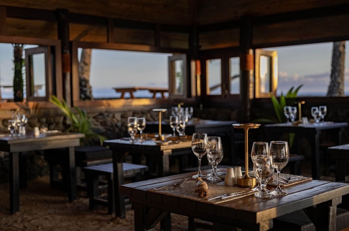 Wine glasses by gold lamps under a dark wooden ceiling near open windows in Wicked Walu at Warwick Fiji Resort and Spa