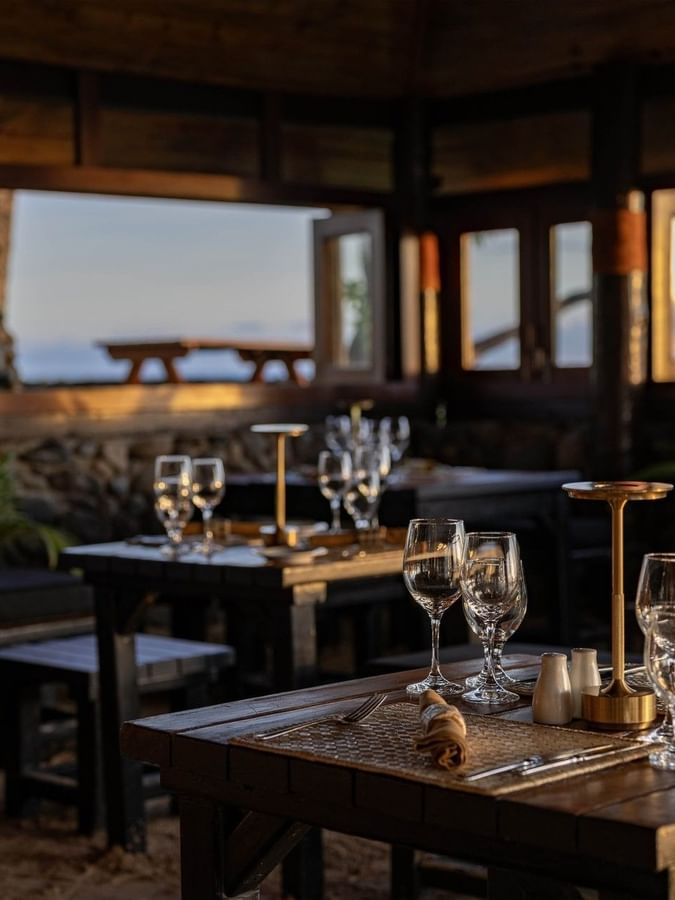 Wine glasses by gold lamps under a dark wooden ceiling near open windows in Wicked Walu at Warwick Fiji Resort and Spa