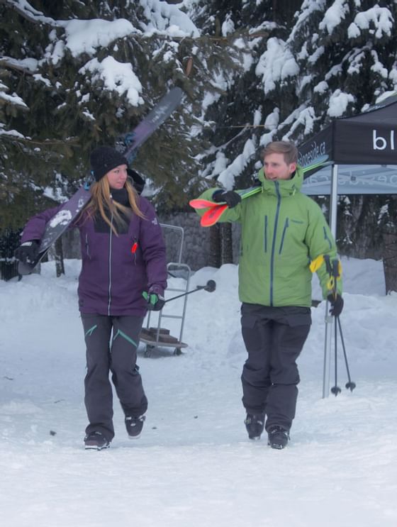 Couple walking on snow while holding snowboarding equipment at Blackcomb Springs Suites