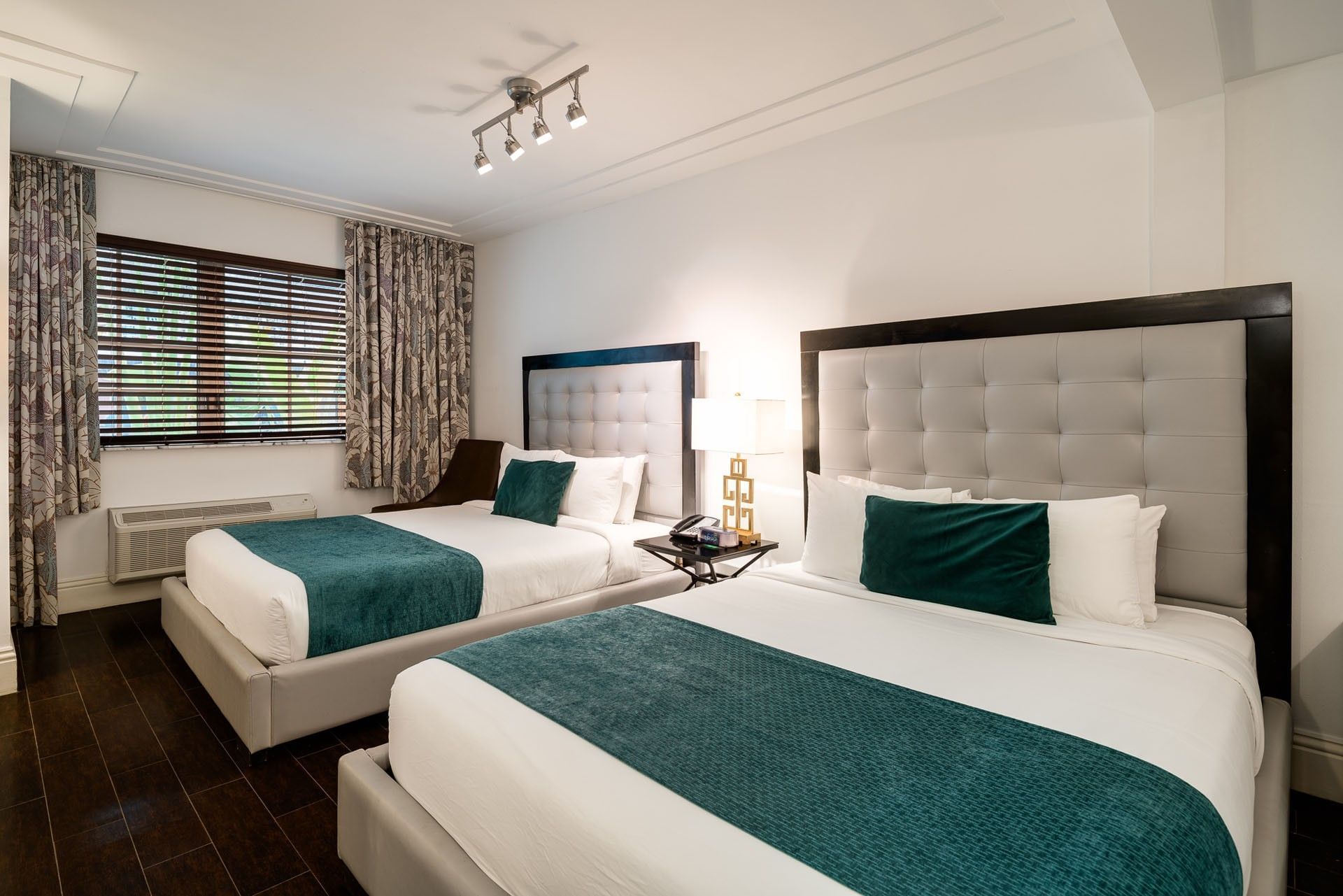 A hotel room with two double beds, tufted headboards, and a window with curtains.
