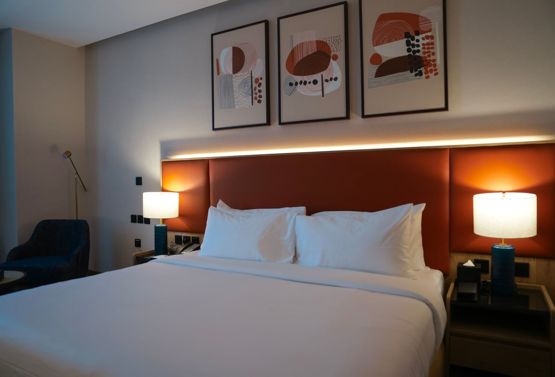 Clean hotel room with a bed, headboard, lamps, chair, and three wall paintings at Warwick Hotel & Spa - Jeddah