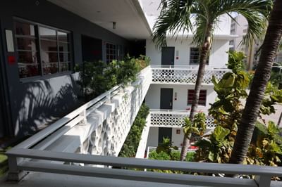 Hotel corridor with gray walls, decorative railings, and lush greenery, featuring room numbers and doors at The Gaythering