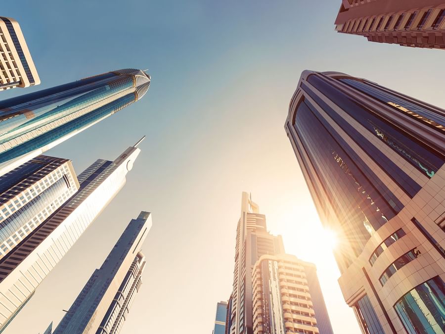 Skyscrapers towering into the sky with sunlight peeking from behind, cityscape view near DAMAC Hotels & Resorts