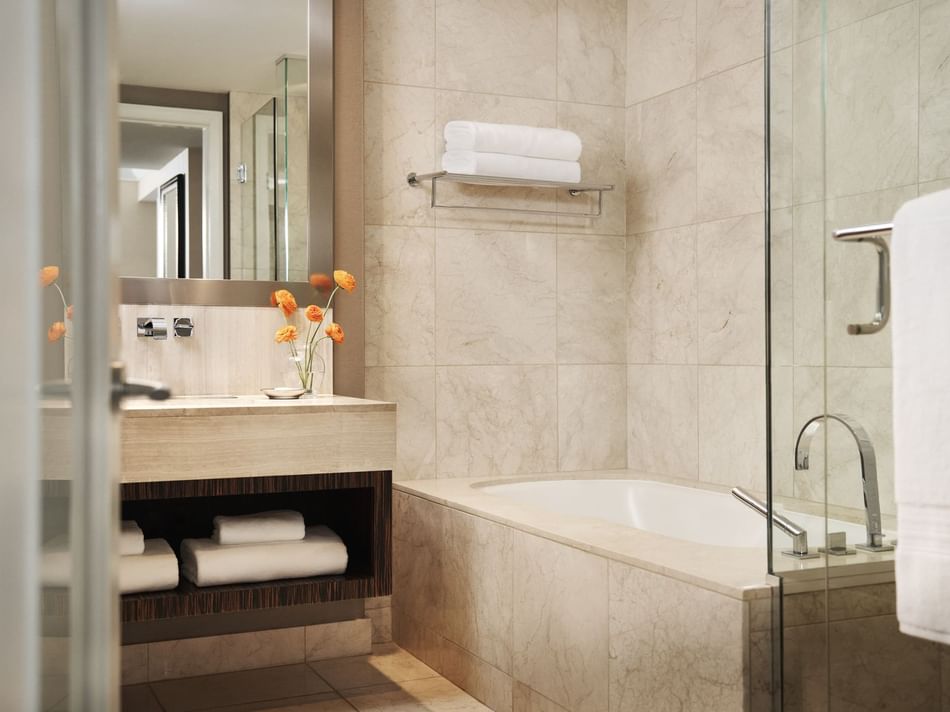 A modern bathroom with a bathtub, shower, and sink, adorned with towels and orange flowers.