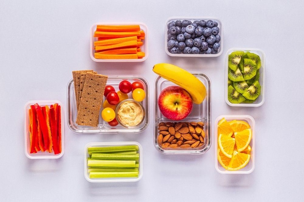 An array of clear Tupperware packed with healthy and colorful snacks. Pack your own food to stick to your budget on spring break. 
