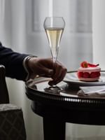 Man holding a champagne glass by a dessert plate at Hôtel Westminster Paris.