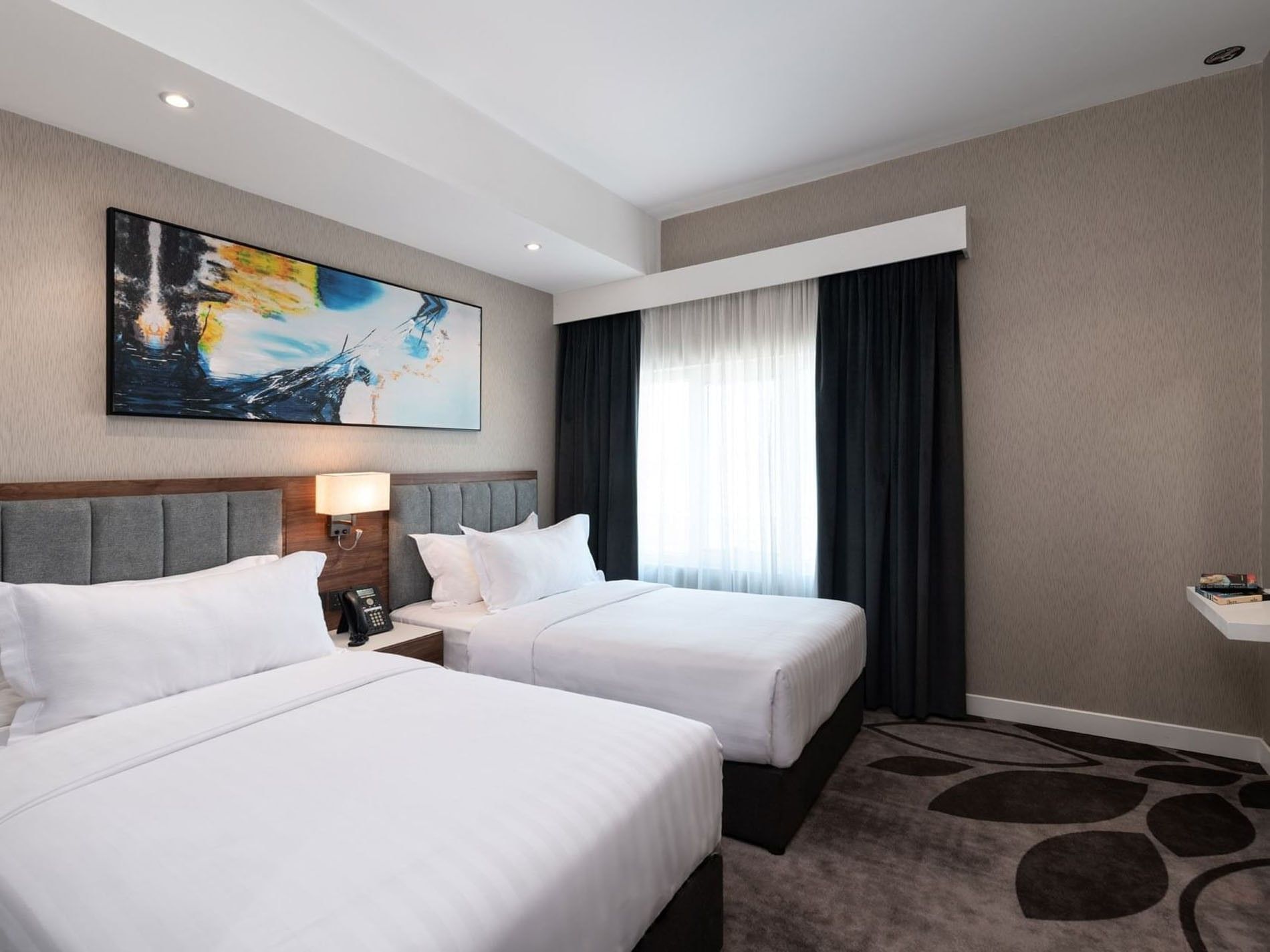 Twin beds with grey headboards under a vibrant abstract blue wall painting in Executive Room at Warwick Al Jubail City View 