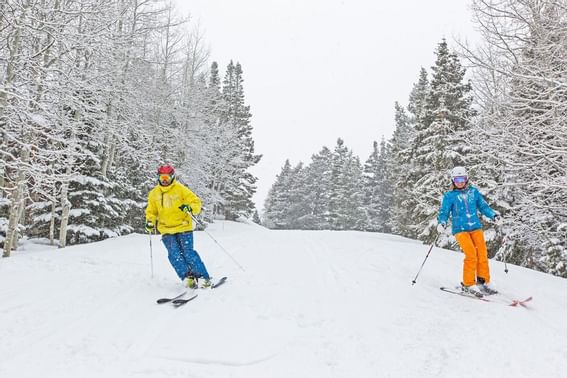 Two skiers by a snowy forest near Chateaux Deer Valley