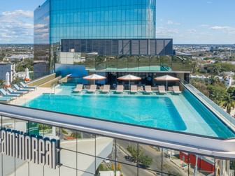 Large rooftop infinity pool featuring blue loungers and a modern glass skyscraper at Camino Real Merida