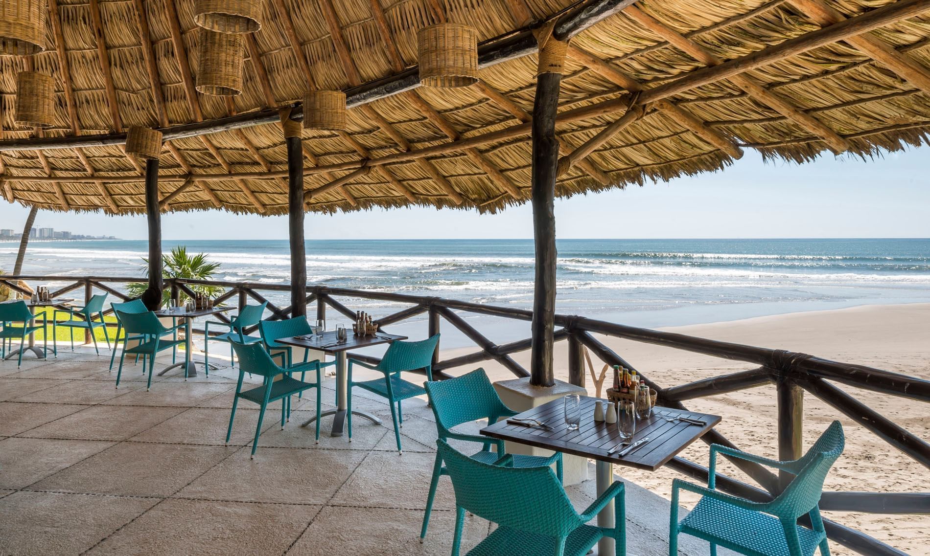 Oceanfront dining in La Bocana with teal chairs under a palapa roof overlooking the waves at Quinta Real Acapulco