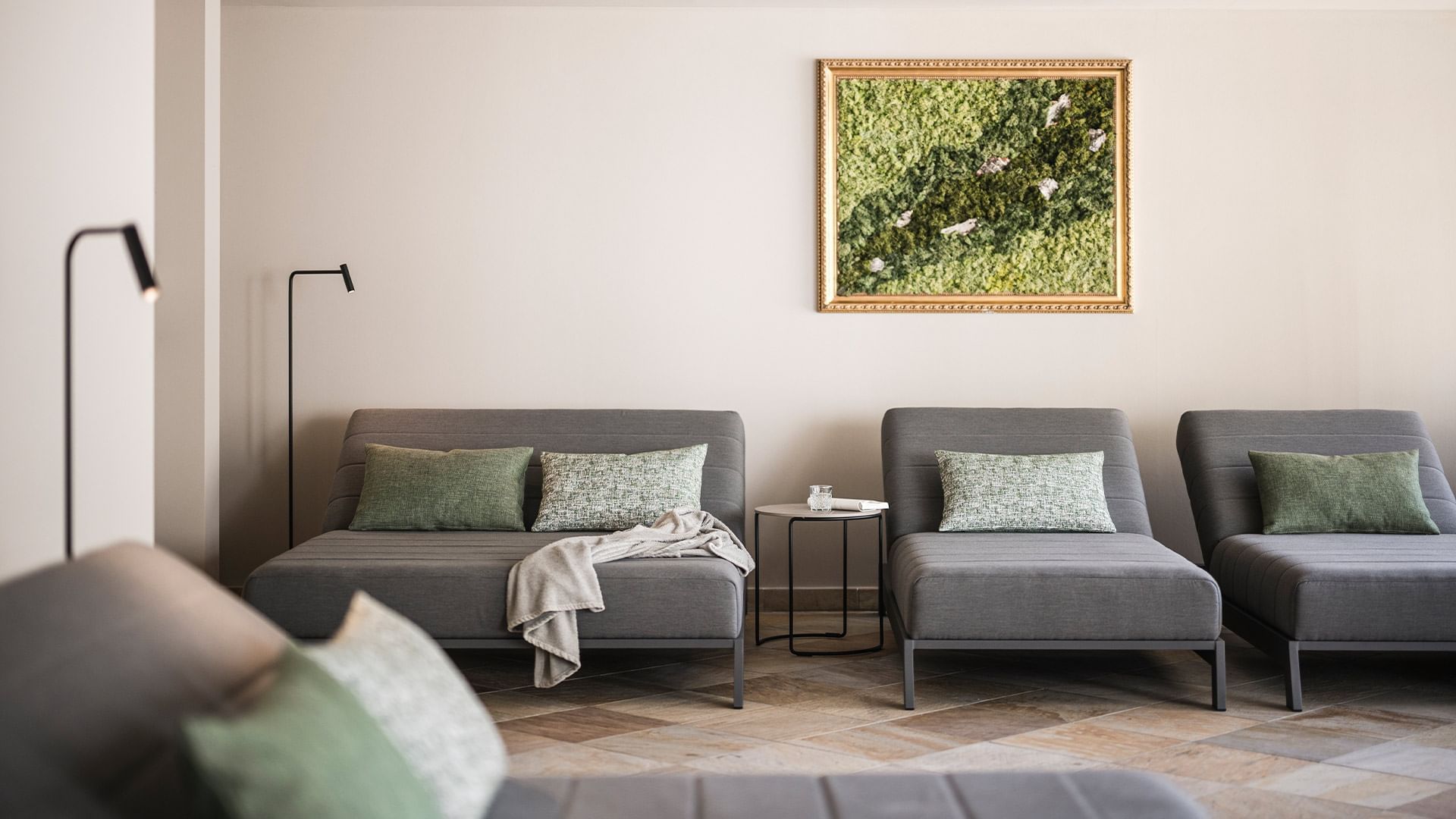 Room with three gray couches, side table, two lamps, and a framed artwork on the wall.