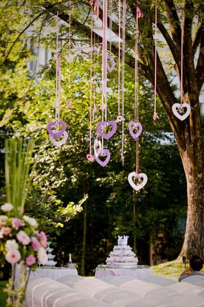 Outdoor wedding at The Saujana Hotel Kuala Lumpur with heart décor, tiered cake, and seating under a lush green tree
