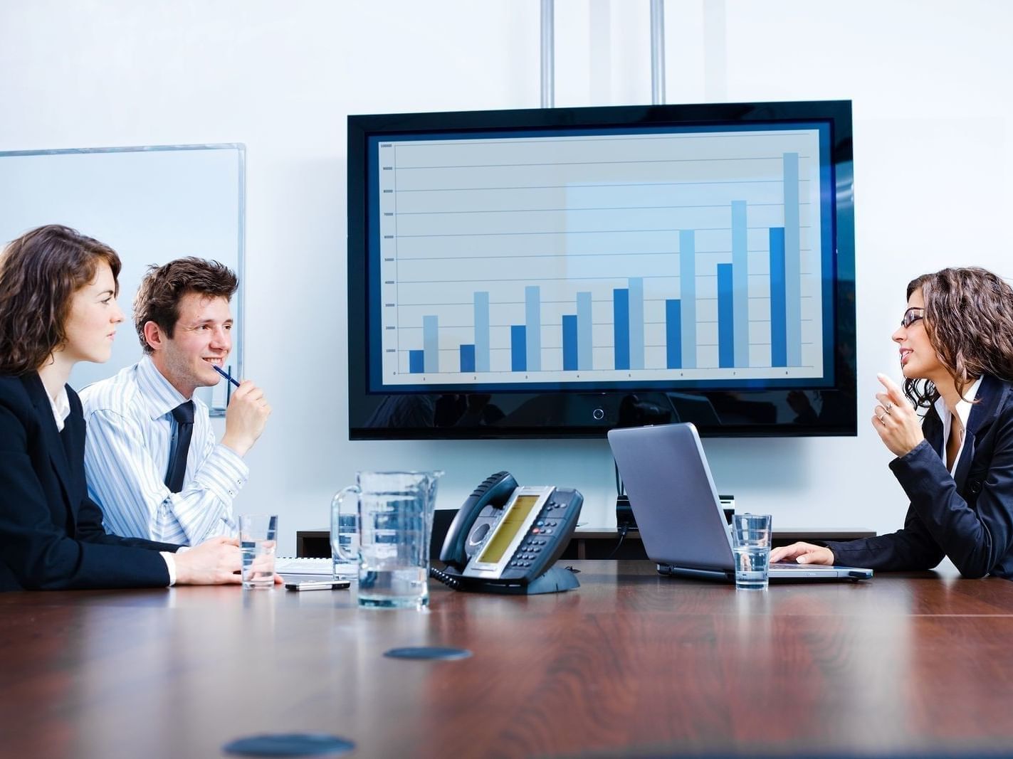 Three professionals discussing, with a large TV displaying a bar graph in the Bear Creek Conference Room at Redmond Inn