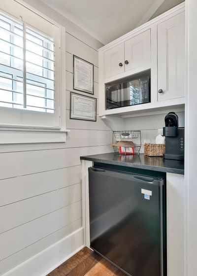 Compact cottage kitchen with black fridge, microwave, coffee maker, and white shiplap walls by Cottages at Laurel Brooke