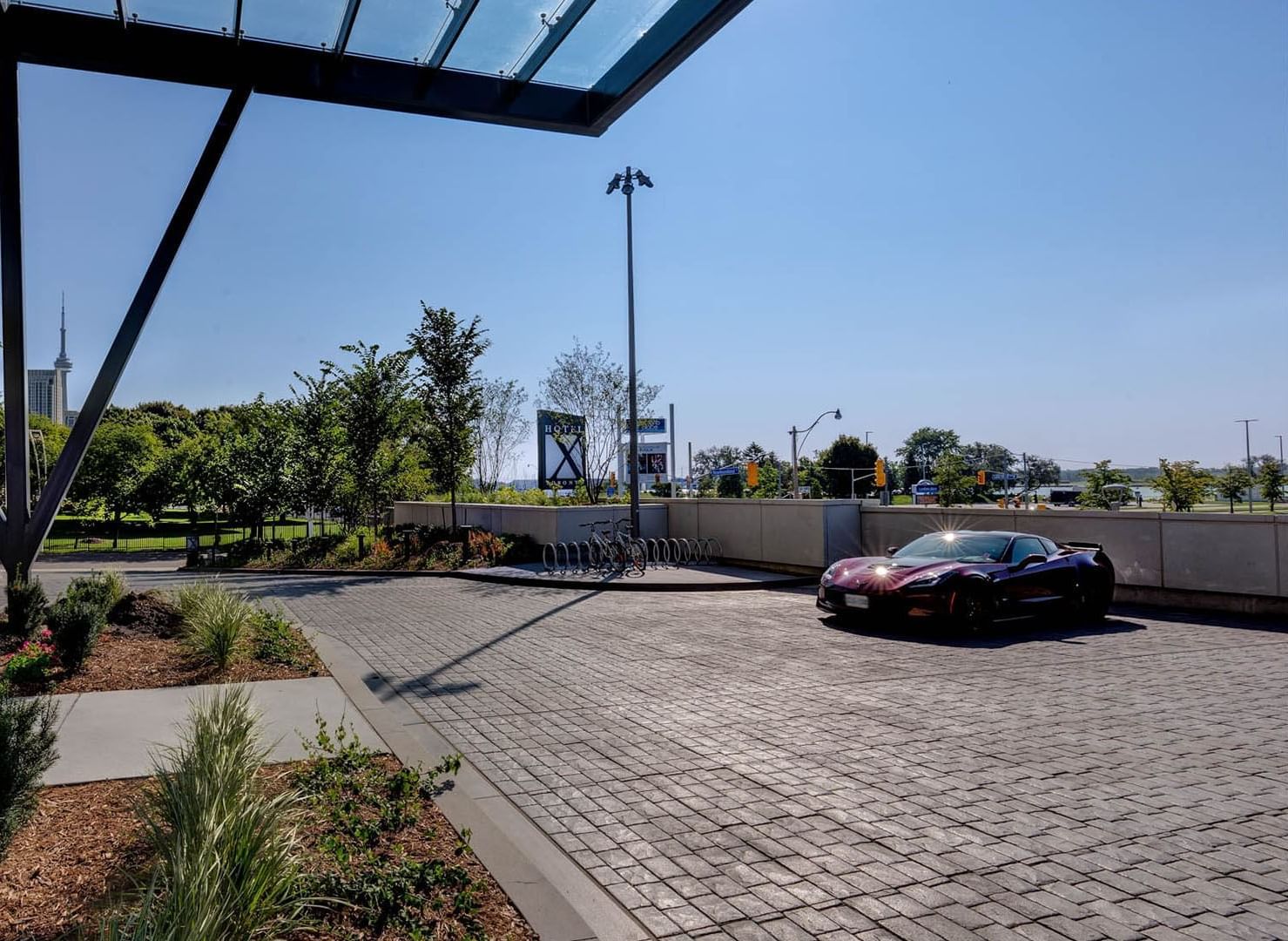 Sleek dark sports car parked on stone driveway facing entrance canopy and city skyline views at Hotel X Toronto
