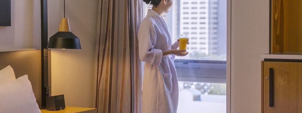 Guest in a robe enjoys a fresh juice by the city view window in the Privilege Room at Mercure Brisbane King George Square