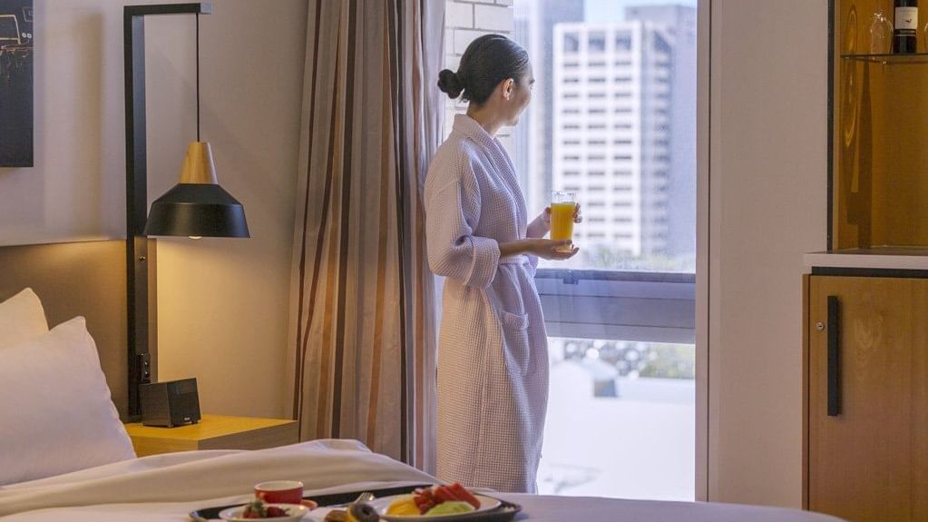 Guest in a robe enjoys a fresh juice by the city view window in the Privilege Room at Mercure Brisbane King George Square