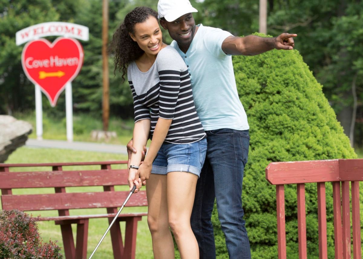Couple cheerily practices mini-golf together in a lush, green outdoor setting at Cove Pocono Resorts