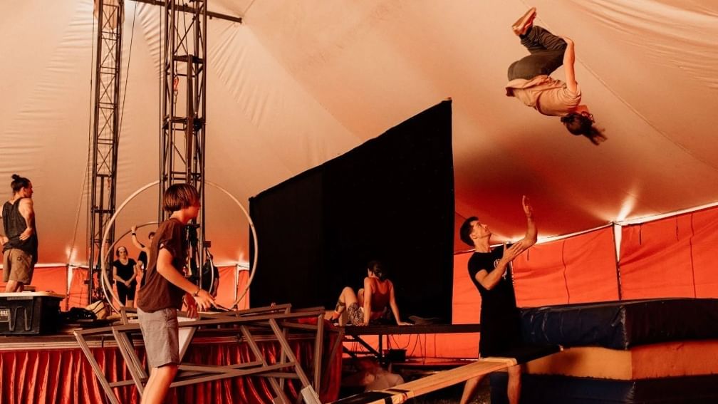 Acrobat performing a mid-air flip onto safety mats under a circus tent at the Karnidale Circus Festival 2027.