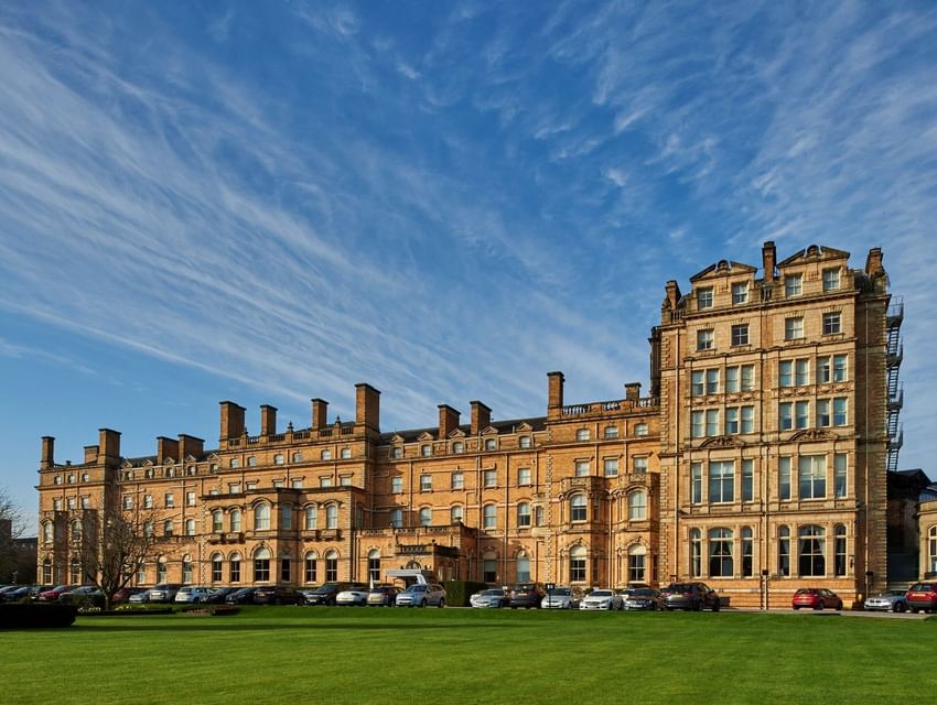 Bright, wide-angle photo of the long stone facade of The Milner York hotel with a lush green lawn in the foreground