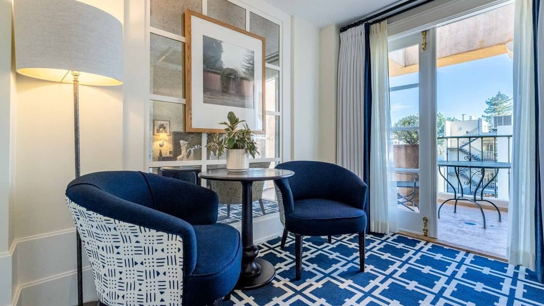 Stylish seating area with blue armchairs and a patterned rug, next to a balcony in Deluxe Queen Room at El Prado Hotel