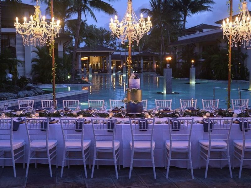 Outdoor evening event setup with chandeliers above tables by pool in Pool Bar Terrace at Pullman Port Douglas