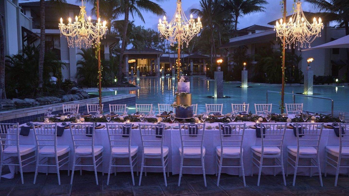 Outdoor evening event setup with chandeliers above tables by pool in Pool Bar Terrace at Pullman Port Douglas