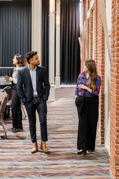 Business people talking while walking down a hallway with patterned carpet and brick walls at the Rodd Royalty