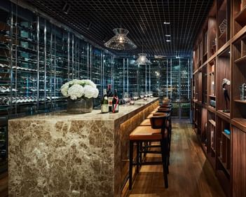 Square One’s wine bar with a marble top, leather stools, glass wine rack, and soft floral accents at Park Hyatt Saigon
