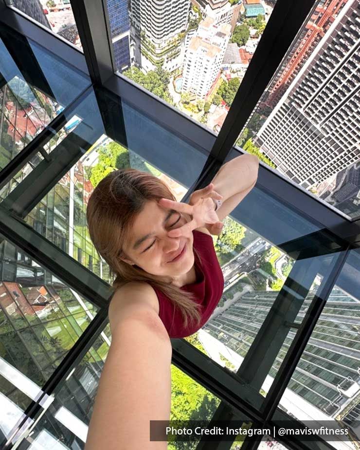 A young woman taking a selfie on a glass observation deck overlooking the ground at Imperial Lexis Kuala Lumpur.