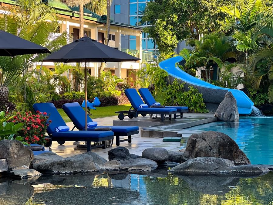 Bright blue loungers under a black patio umbrella by a winding swimming pool at TokaToka Resort Nadi Fiji