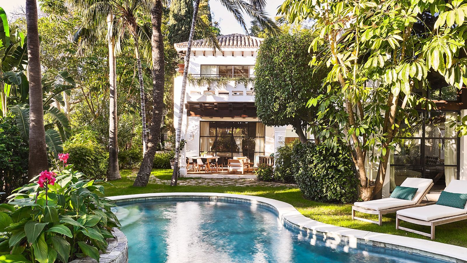 Villa with a second-floor balcony overlooking a curved swimming pool set in a lush garden at the Marbella Club