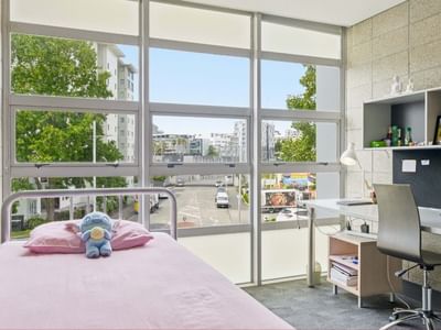Pink bed and desk with city view through large windows at Student Living Auckland - Beach.