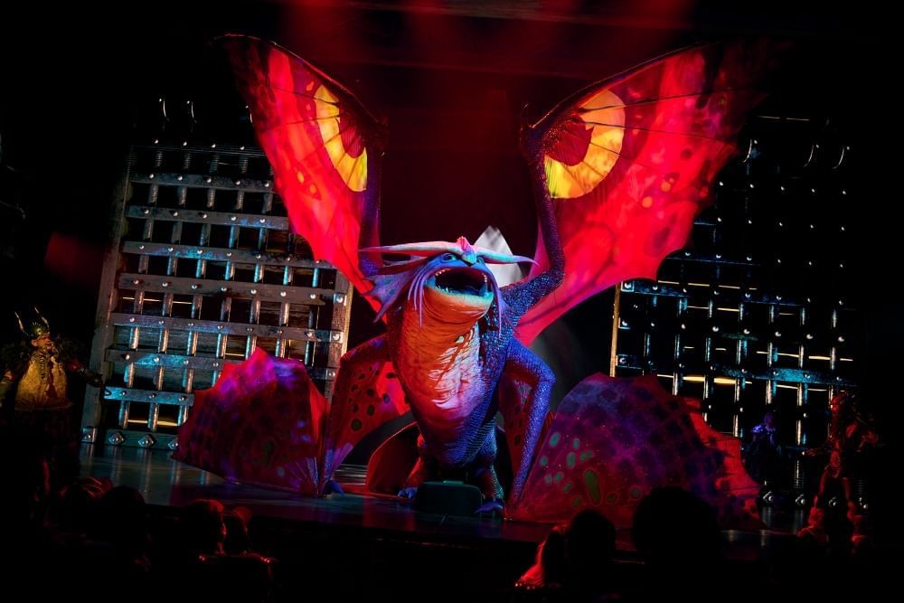 A large purple dragon with fiery red wings bellows on a dark stage. 