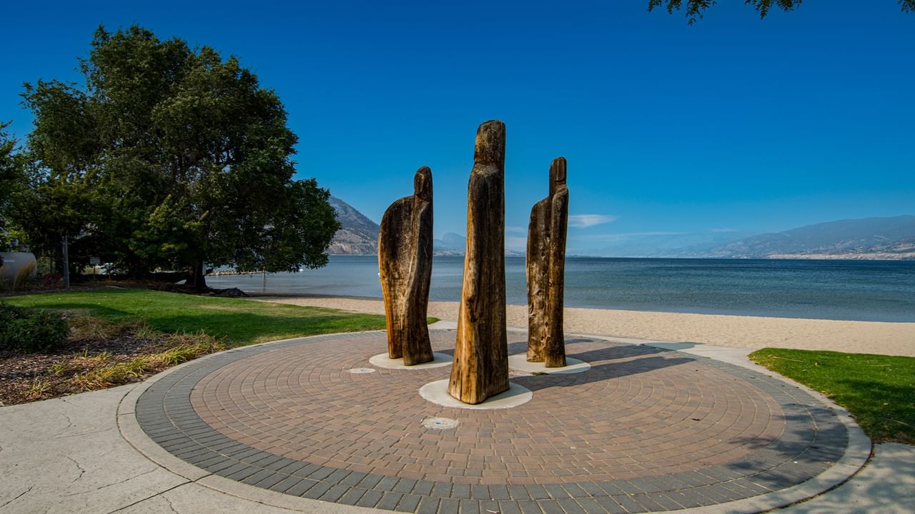 Three wooden figures on a circular brick platform near Okanagan Lake.