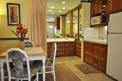 Suite interior with a dining table, kitchenette, and a mirrored vanity area in the background at Americana Village Suites