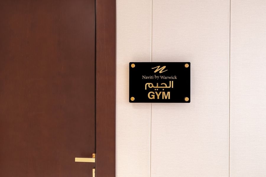 Black acrylic Gym door sign plaque with Arabic script mounted on wall beside wooden entryway at Naviti by Warwick Jeddah