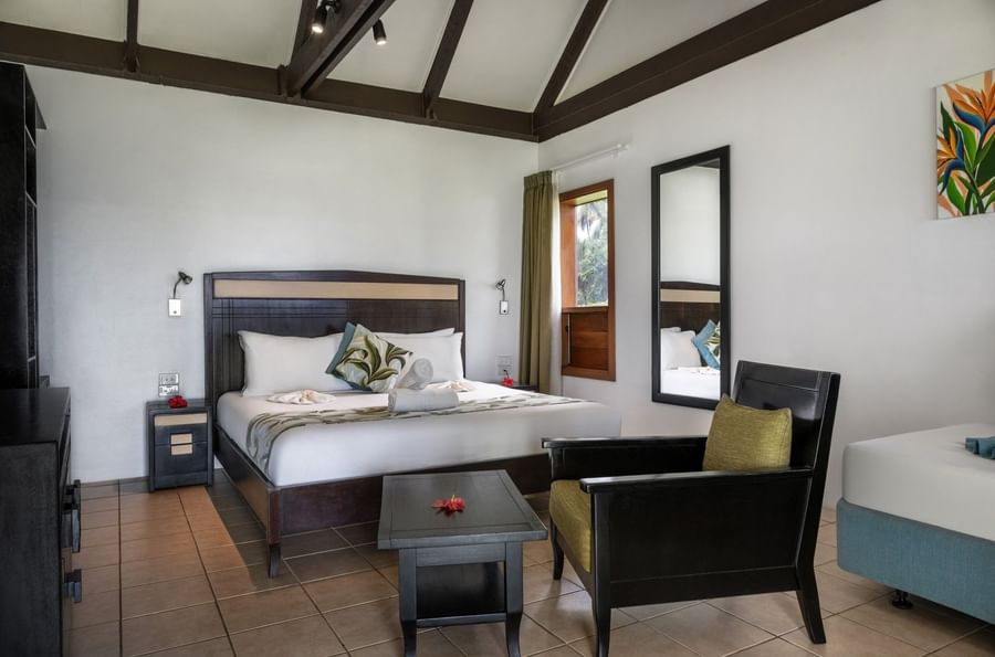 Wooden bed by a black armchair and coffee table with beams in Ocean View Villa at Tambua Sands Beach Resort