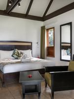 Wooden bed by a black armchair and coffee table with beams in Ocean View Villa at Tambua Sands Beach Resort